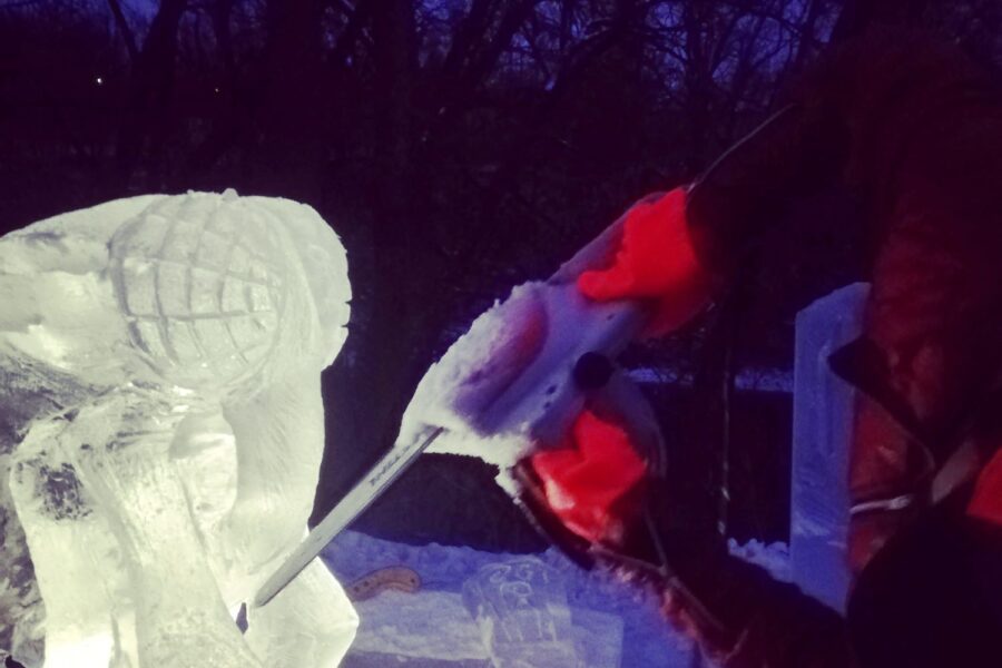 Un homme sculpte un bloc de glace avec une scie en hiver à la tombée du jour.
